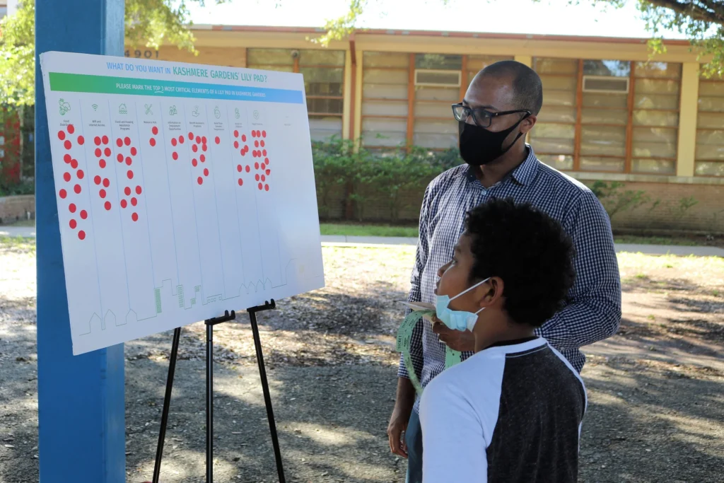 Boy and adult looking at a board with dot stickers grouped by the community's interests in an upcoming project