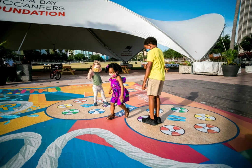 Young children playing on a large-scale board game in a public plaza