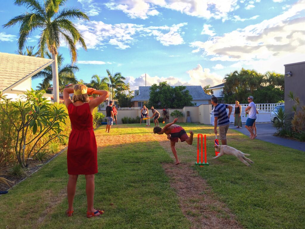 People playing cricket together in a sunny backyard in Australia.