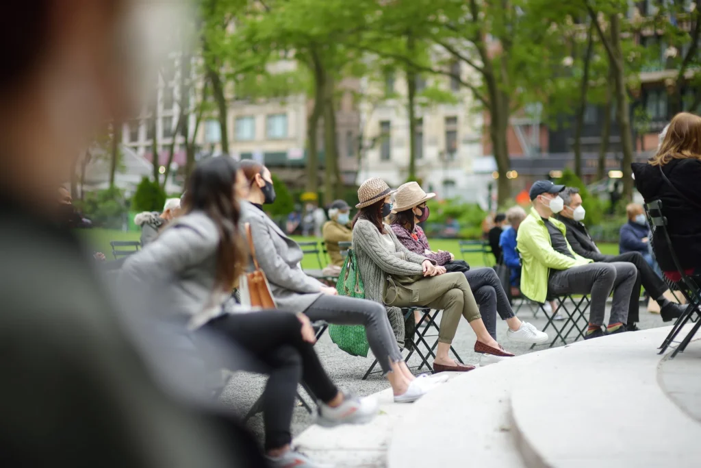 Several people sitting in public benches wearing face masks in Bryant Park, NY